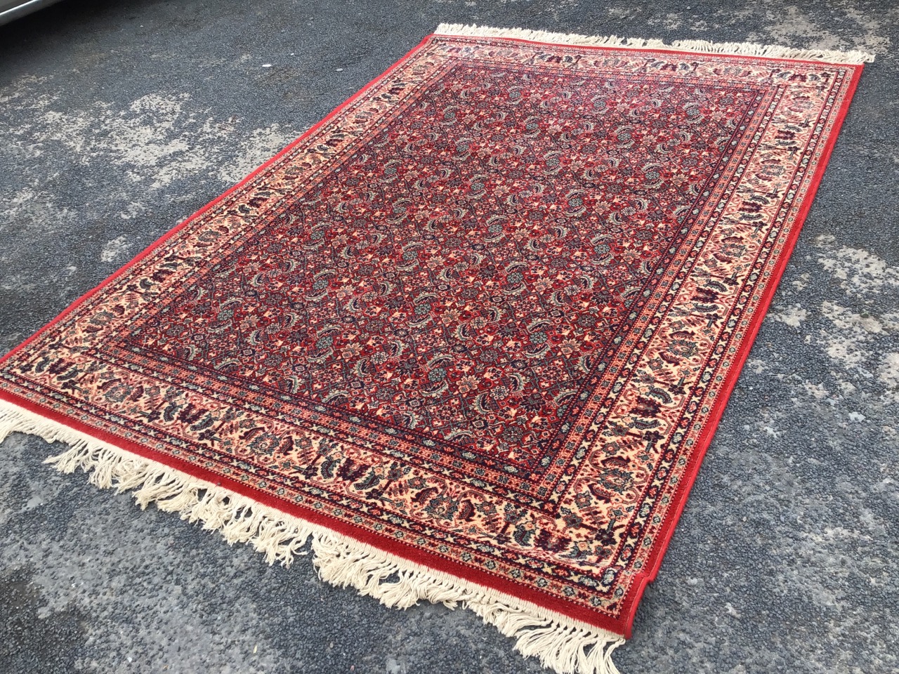 A Persian rug woven with field of busy paisley type floral decoration on red ground, within a frieze