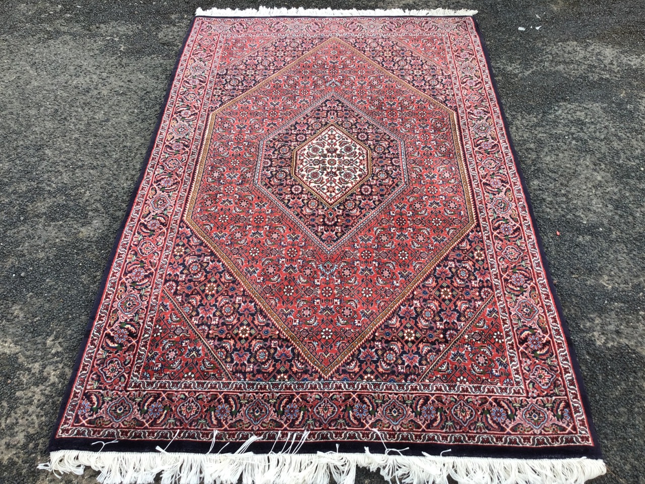 A Kashan style rug woven with multi-floral field centering on a diamond shaped medallion, the frieze