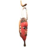A painted African tribal art mask, the elongated head surmounted by a tapering hook, with ribbed