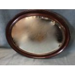 An oval Edwardian framed mirror with bevelled plate in grained concave ribbed frame, having