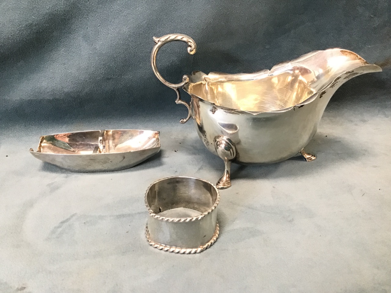 A hallmarked silver gravy boat with scrolled handle - London, 1909; a napkin ring with rope style