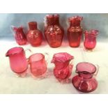 A collection of Victorian cranberry glass jugs, fluted, crimped handles and feet, wave rimmed, all