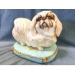 A large ceramic pug dog, the hand glazed brown eyed beast standing on gilt tasseled cushion. (17.