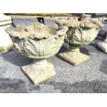 A pair of circular leaf moulded composition stone garden urns with scalloped rims, raised on