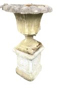 A composition stone garden urn on stand, with lobbed rim above a fluted body on socle with square