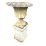 A composition stone garden urn on stand, with lobbed rim above a fluted body on socle with square