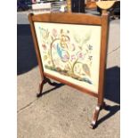 A C20th mahogany firescreen with arched frame and glass enclosing a fine crewelwork panel on linen