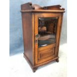 An Edwardian oak smokers cabinet with shaped gallery to top above a bevelled glass door enclosing