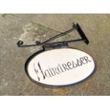 A wall mounting hanging shop display sign, with oval painted panel swinging on scrolled bracket,