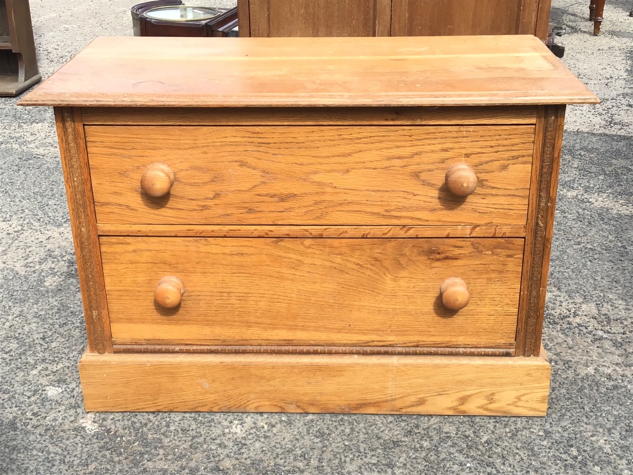 A low C20th oak chest of two knobbed drawers, with rectangular moulded top flanked by carved stiles,