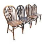 A set of four C20th elm wheelback chairs with pierced splats framed by spindles beneath hoops, the