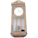 A 30s oak cased wallclock, the arched crest with applied scrolled decoration above a door framed