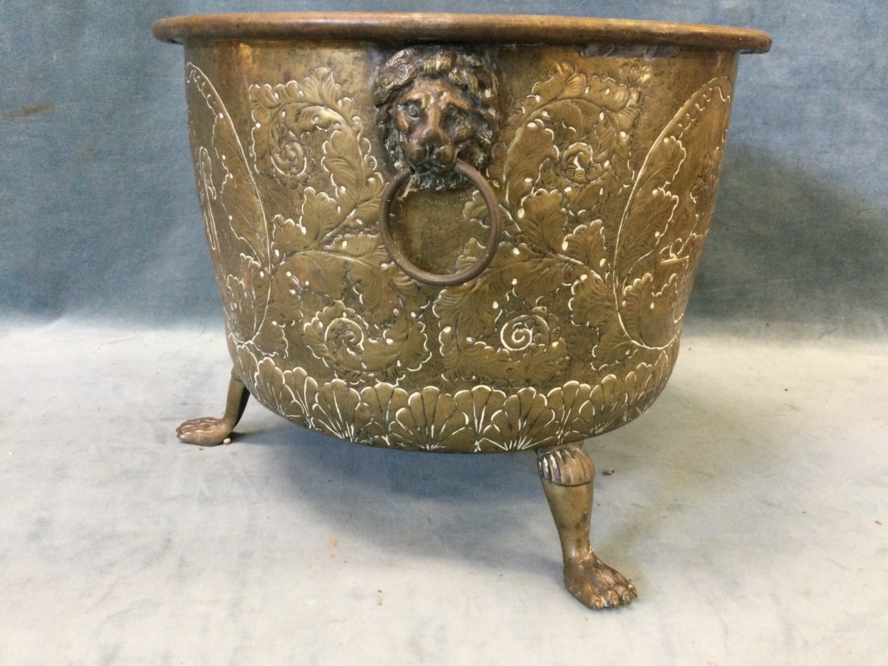 A nineteenth century embossed brass log bin raised on paw feet, the sides with lionmask ring handles