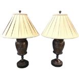 A pair of large bronzed tablelamps with pleated shades above vases on stands, the vessels with