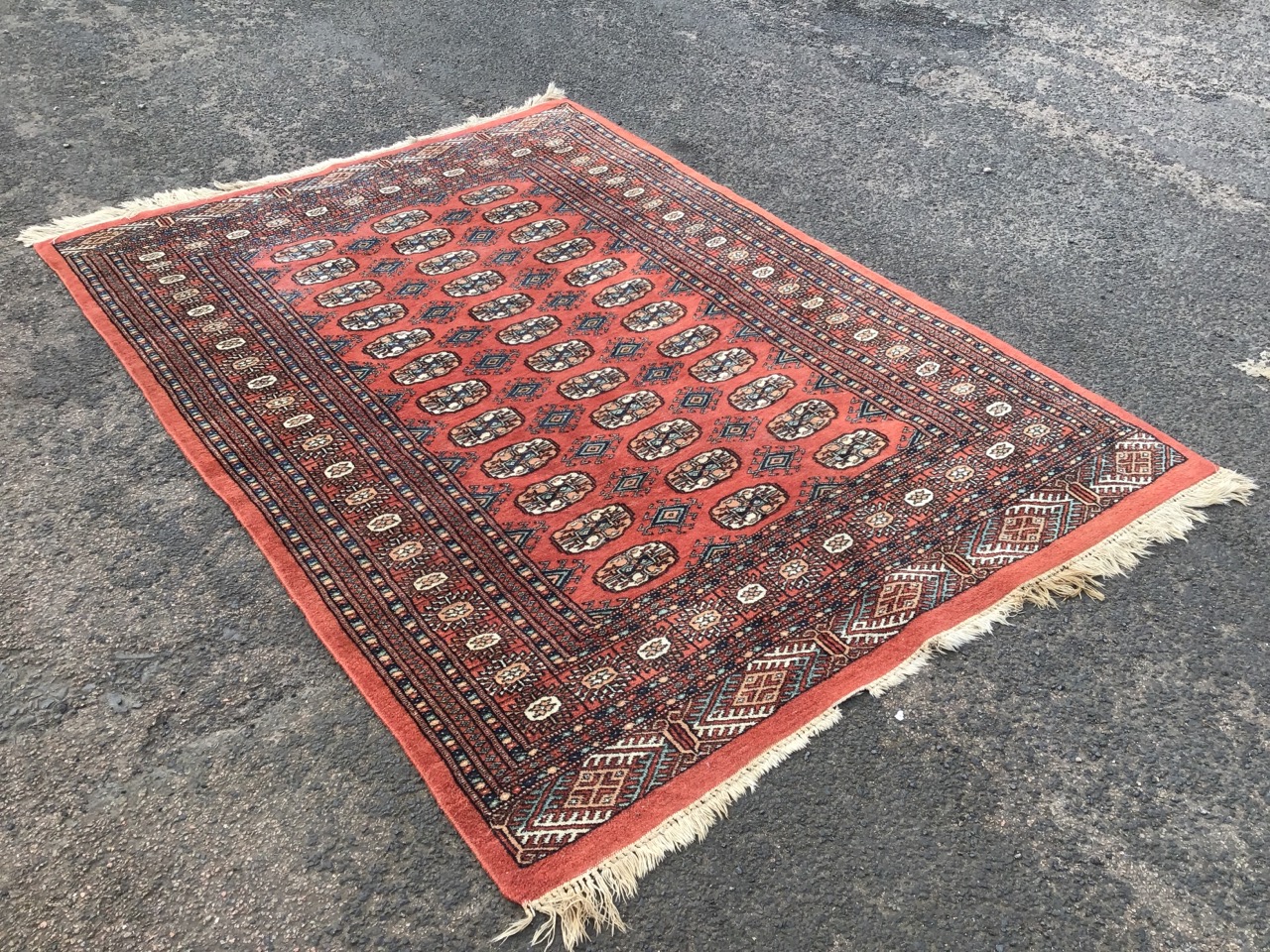 A bokarra type oriental rug woven with madder field of oval lozenges and hooked diamond