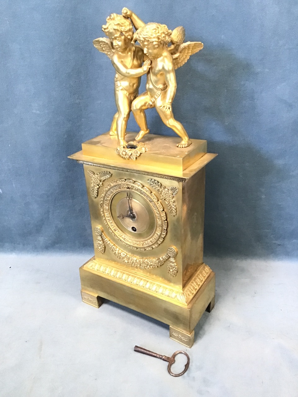 An early 19th century French ormolu clock, surmounted by a pair of startled putti, the egg & dart
