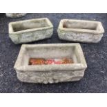 A set of three composition stone garden troughs, the sides moulded with lionheads joined by floral