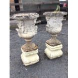 A pair of composition stone garden urns on associated stands, the classical pots with friezes of