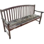 A teak country house garden bench with arched slatted back above a batten seat framed by shaped