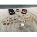 A tin of miscellaneous costume jewellery including brooches, pins, earrings, badges, a hallmarked