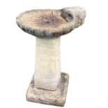 A composition stone garden birdbath, the bowl moulded in the shape of a shell, raised on square