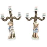 A pair of continental porcelain candelabra with three urn-shaped candleholders above a boy and a
