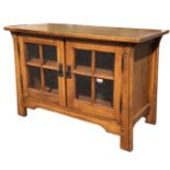 An art nouveau style oak cabinet with rectangular top above glazed doors and shaped apron, supported