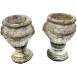 A pair of composition stone garden urns with cushion moulded rims above bodies cast in relief with