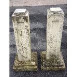 A pair of square composition stone pillars with chamfered panels, raised on stepped bases. (29.75in)
