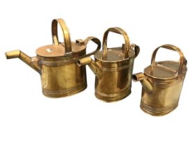 A graduated set of three Victorian brass watering cans, the rounded vessels with ribbed bands having
