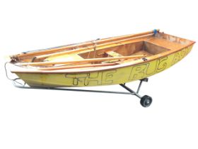 A 20ft sailing dingy, the painted mahogany ply boat complete with mast, oars, boom, etc., mounted on