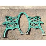 A pair of cast iron garden bench ends with pierced scrolled arms and frames, raised on chanelled