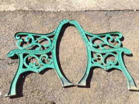 A pair of cast iron garden bench ends with pierced scrolled arms and frames, raised on chanelled