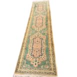 A Persian style wool runner, the green field with three floral medallions and scrolled foliate