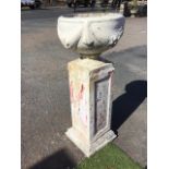 A white painted composition stone urn decorated with fabric and fruit swags, on a square base,