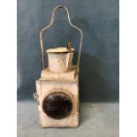 A painted railway lamp with circular red lens to hinged door beneath a chimney with hinged cap and