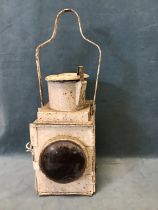 A painted railway lamp with circular red lens to hinged door beneath a chimney with hinged cap and