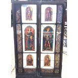 A pair of stained glass doors in grained frames enclosing six arched portrait panels of saints,