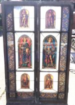 A pair of stained glass doors in grained frames enclosing six arched portrait panels of saints,