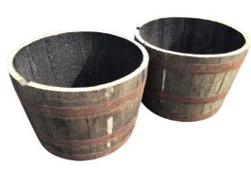 A pair of oak garden barrel tubs, each having staves framed by three riveted metal strap bands. (