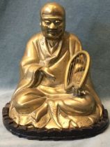 A brass buddha seated cross legged with harp, mounted on carved shaped hardwood stand with