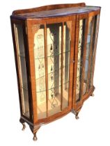 A 1950s serpentine fronted walnut display cabinet, the shaped back above glazed doors with carved