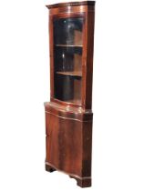 A mahogany serpentine fronted corner cabinet, the dentil cornice above a glazed door enclosing