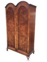 A twin-domed walnut wardrobe with moulded cornice above panelled doors enclosing hanging space,