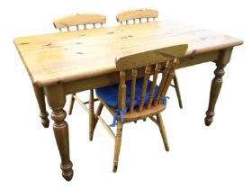 A reproduction rectangular pine kitchen table with three spindleback chairs, the table with frieze