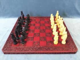 A chess set with figures cast as Chinese royal characters, on a square red lacquered board framed by