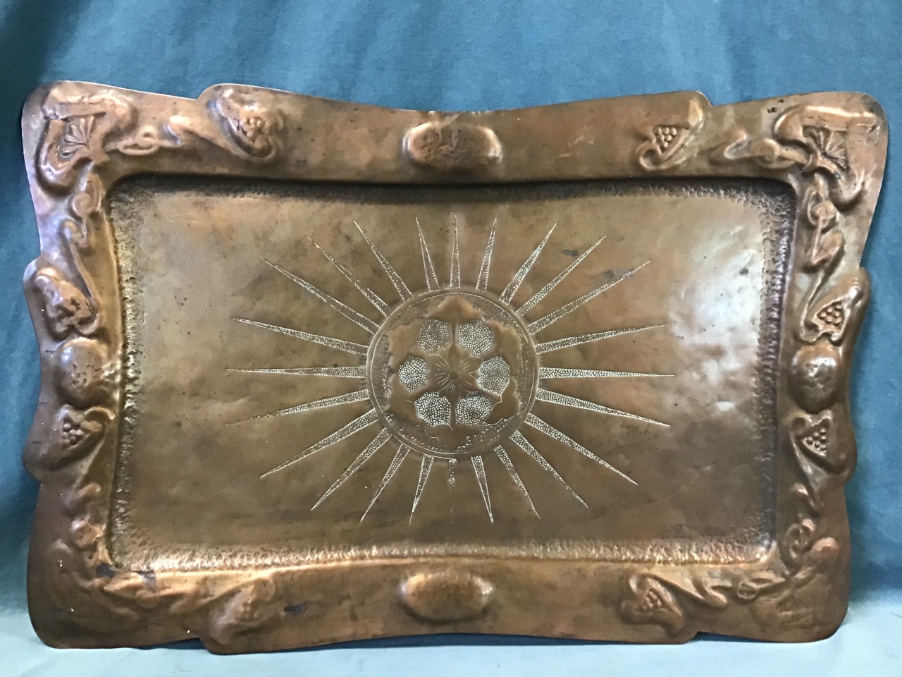 An Edwardian hand-beaten art nouveau copper tray, with central flowerhead and sunburst motif