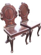 A pair of Victorian mahogany hall chairs, the circular panelled backs within scrolled cartouches