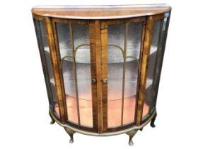 An art deco bowfronted walnut display cabinet, the top with raised back above a pair of sliding