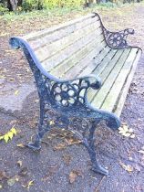 A slatted garden bench with circular pierced floral medallions beneath scrolled arms, supported on